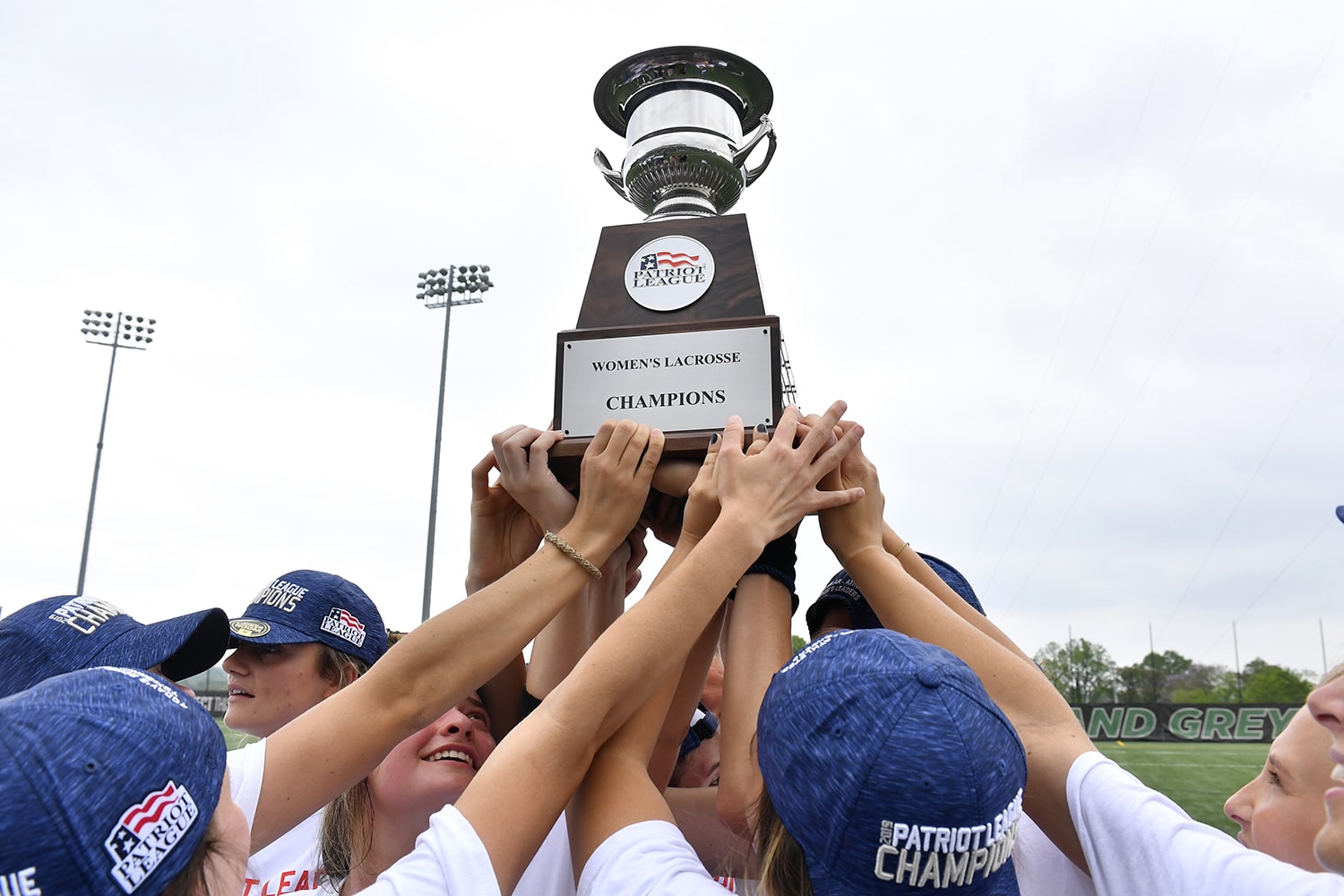 Student athletes from the Women's lacrosse team holding up the Patriot League championship trophy