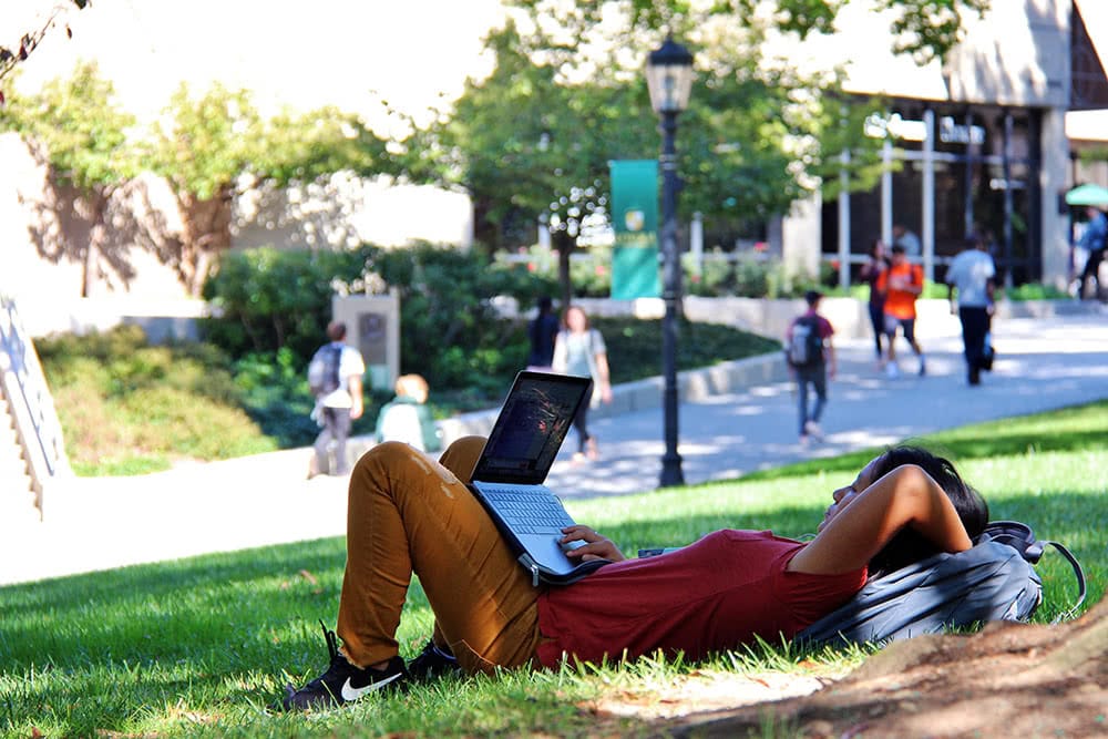 A student laying on the grass with a laptop in her lap