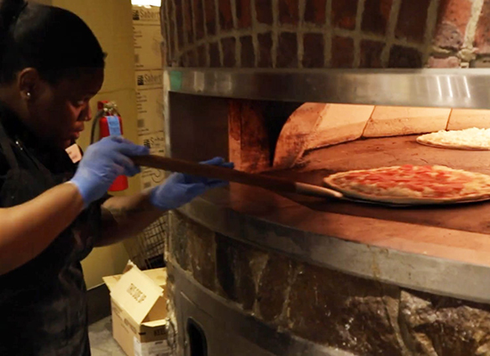 Dining services employee pulling pizza out of brick oven at Iggy's Market