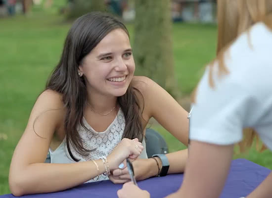 A female student smiles at another student while sitting at a table on Loyola's academic Quad