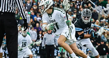 A Loyola lacrosse player with the ball runs past a Johns Hopkins player
