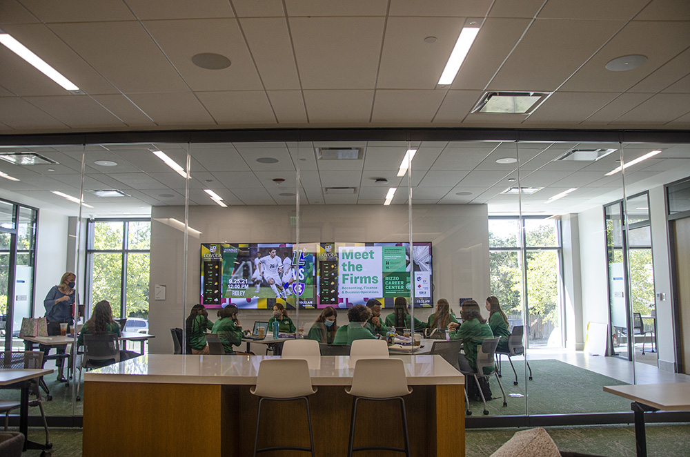 Students huddle around a table with a large display screen during a meeting