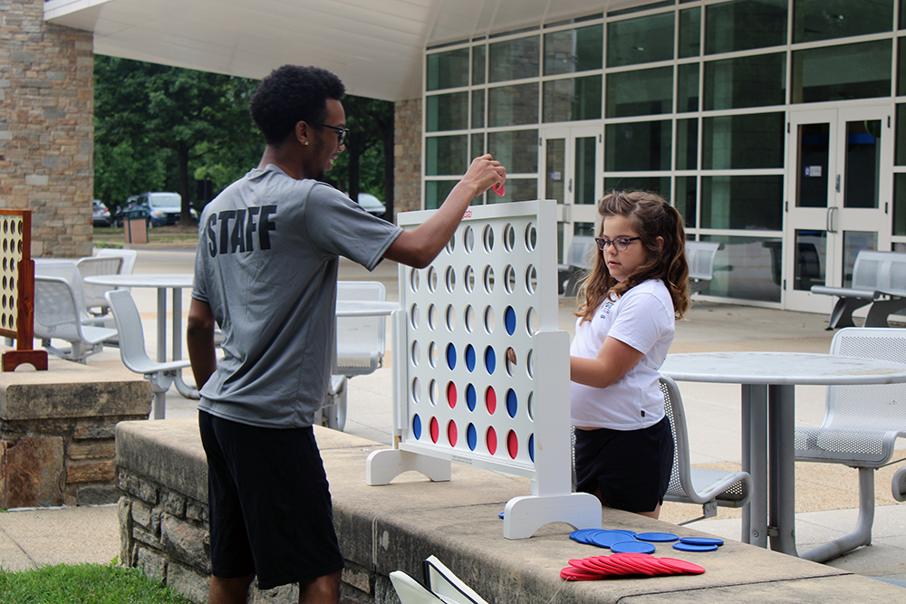 A male counselor plays a jumbo version of Connect Four with a camper outside