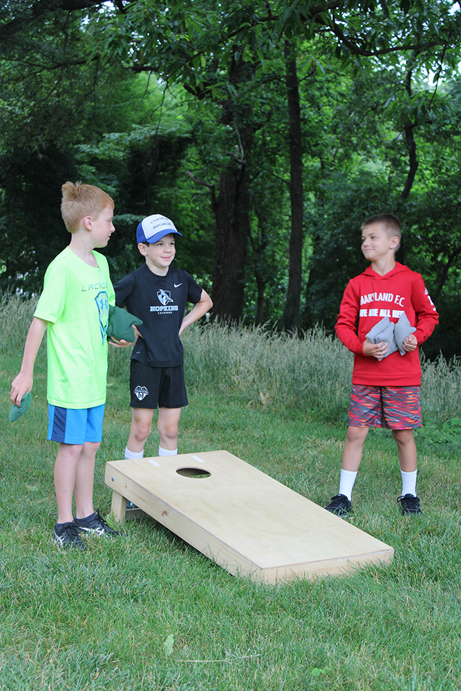 Three male campers play cornhole on the lawn outside Loyola's Fitness and Aquatic Center