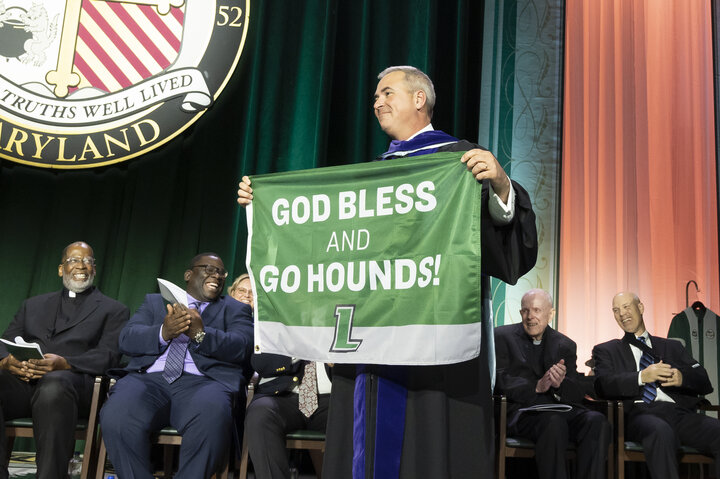 Loyola’s 25th president, Terrence M. Sawyer, J.D., holds a “God Bless and Go Hounds flag” at the Inauguration Convocation