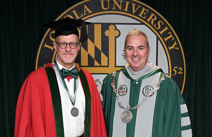 Dressed in academic regalia, Loyola College Dean Stephen Fowl stands with President Terrence Sawyer in front of the Loyola University Maryland seal