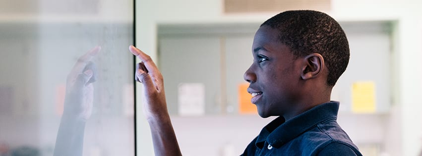 A male student interacting with a touchscreen in a classroom