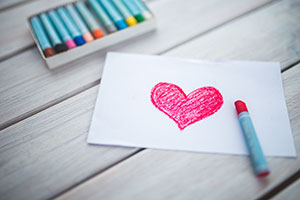 Paper with a red heart and crayons on a table