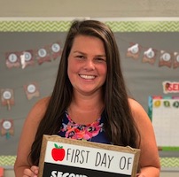 Allison Glace, dark-haired woman holding a sign 'First day of second grade'