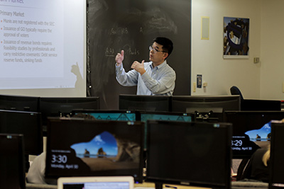 A professor teaching in front of a blackboard and projection screen