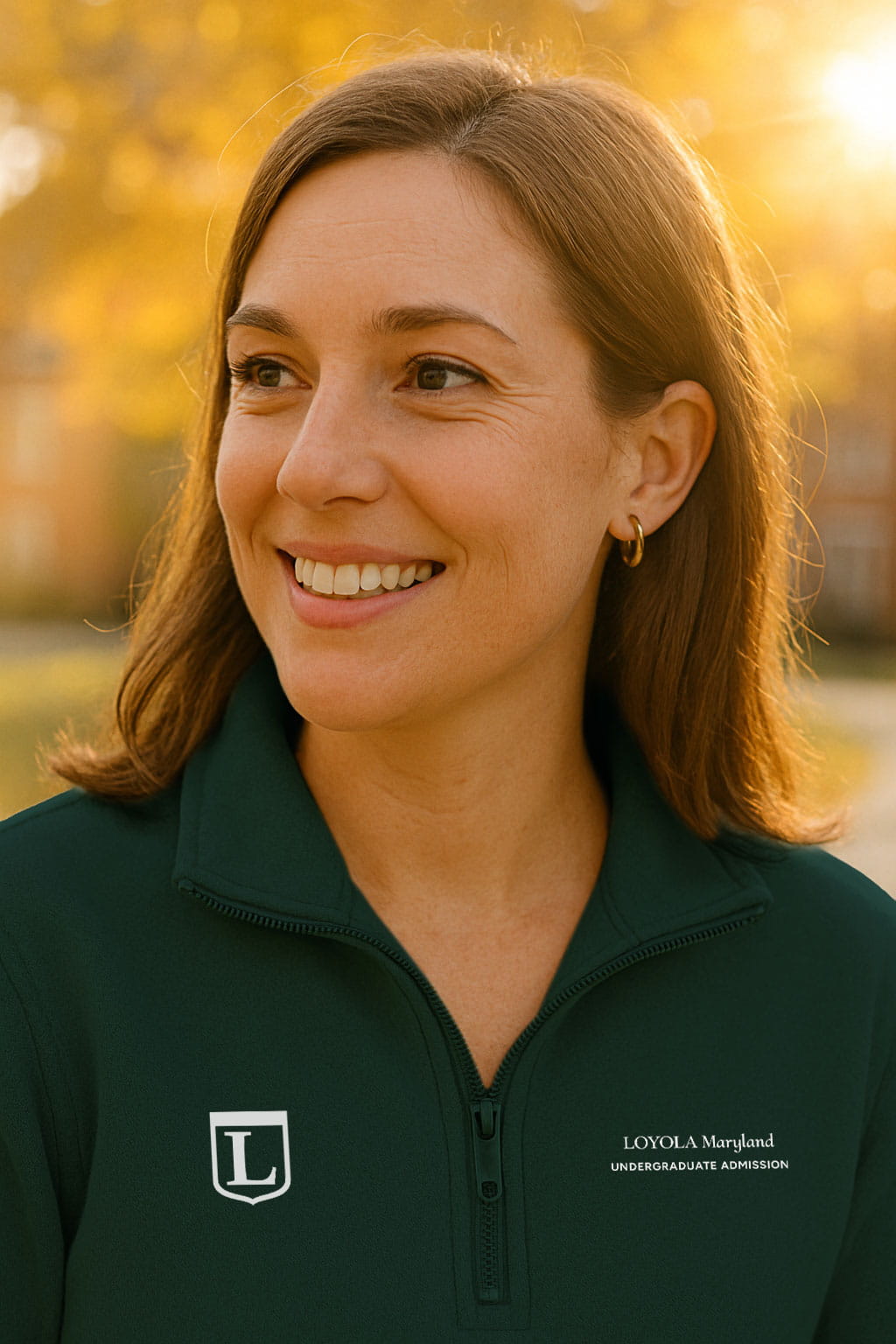 A woman smiling on campus wearing a Loyola polo shirt with the monogram on the left and extended wordmark on the right.