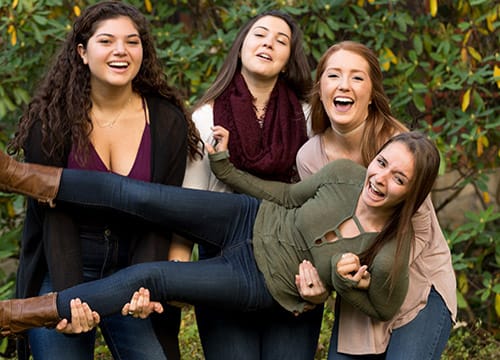 Three female students holding a fourth student, all smiling and laughing