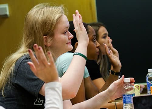 Students sitting in class and raising their hands to answer a question