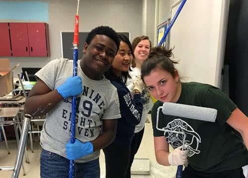 Students holding painting tools in a school classroom