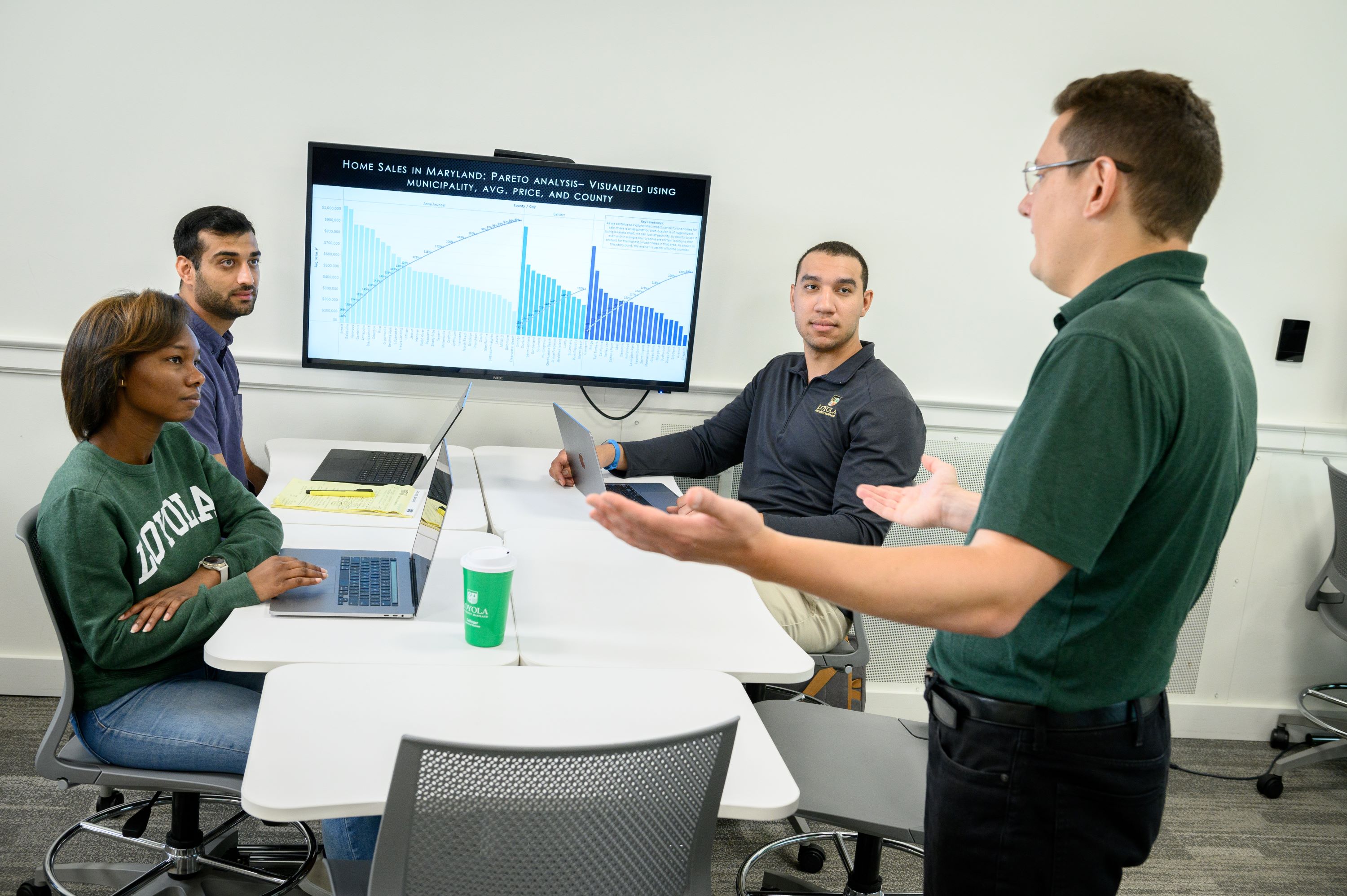 An instructor speaks to a group of students at a table.