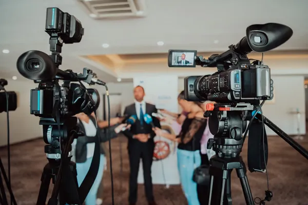 Two cameras pointed toward an individual in a suit being interviewed
