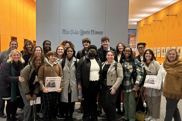 A class photo taken in front of a sign reading: The New York Times