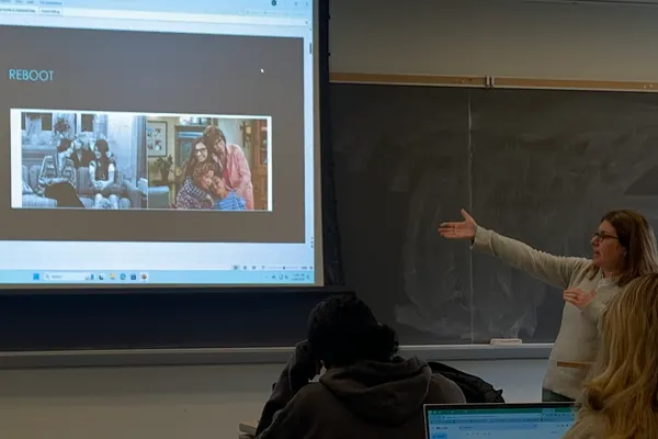 A professor lecturing and pointing at a slide on the projection screen.