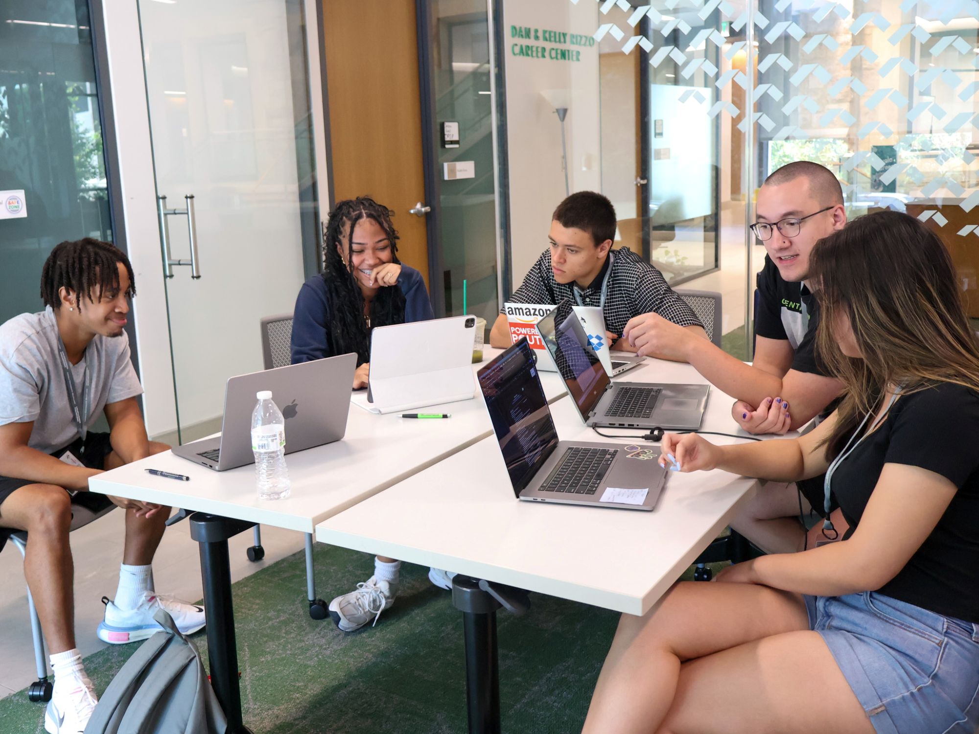 Students sit together at tables with laptops open while working together. 