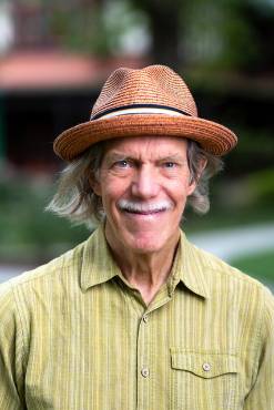 A headshot of John Casey in a green shirt and brown hat
