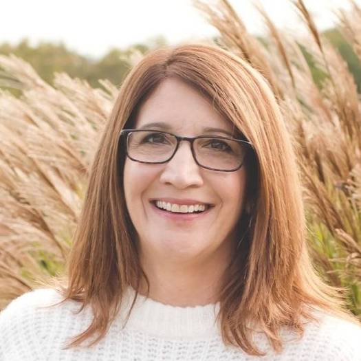 Terri Allen headshot with glasses in white sweater with wheat background