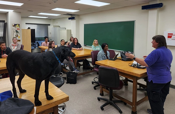 Teacher works with students in the classroom. Photo also features a dog for the lesson