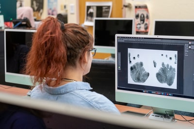 Student examines ink hand prints on a monitor in a computer lab