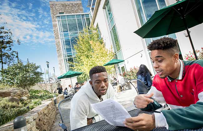 Two students looking over a paper together on the Student Center patio on a sunny day