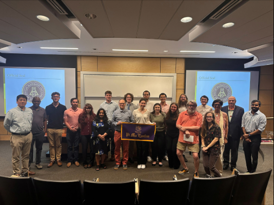 Group of Pi Mu Epsilon members standing together holding the banner