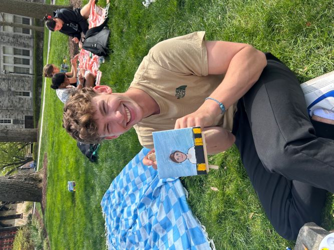 college student poses with small painted portrait of himself