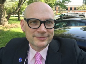  Alex Young, a man wearing glasses, a suit, and a pink tie.