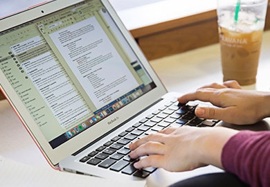 Closeup shot of student typing on laptop next to a Starbucks coffee