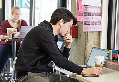 Student looking intently at his laptop screen in the Student Center with a Starbucks coffee