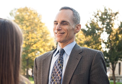 Faculty member in a suit smiling while talking with a student on campus