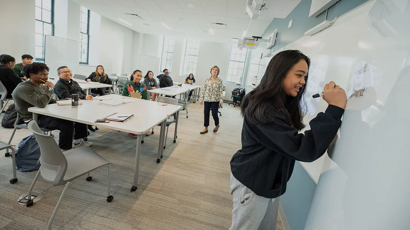 A student writes on a whiteboard while other students watch - Press enter to play