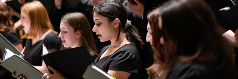 A choir singing with members holding open black folders.