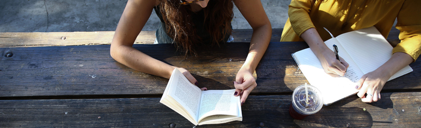 two students reading and writing on picnic table