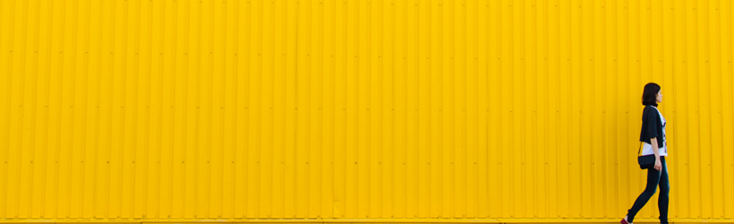 student walking in front of bright yellow wall