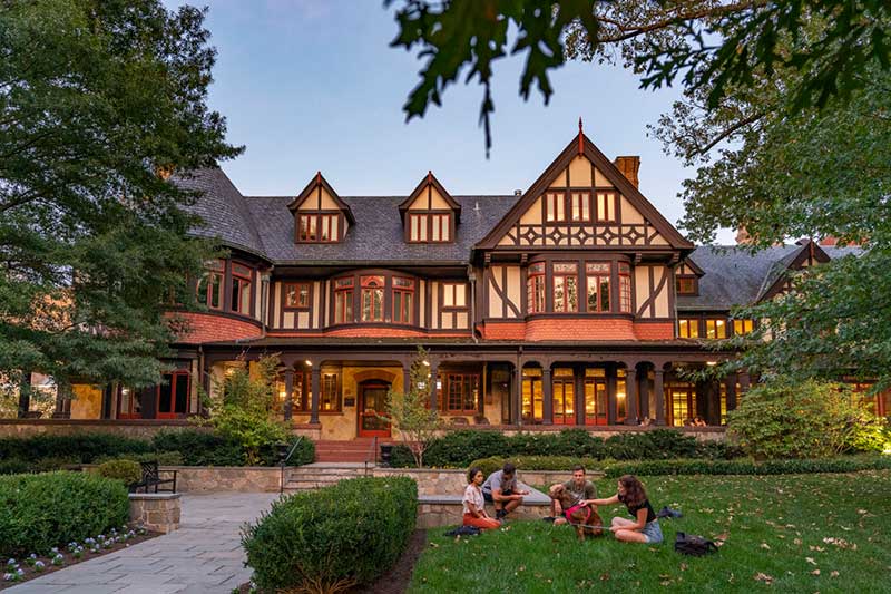 A group of students spread out on the grass by the Tudor-style Humanities building at dusk