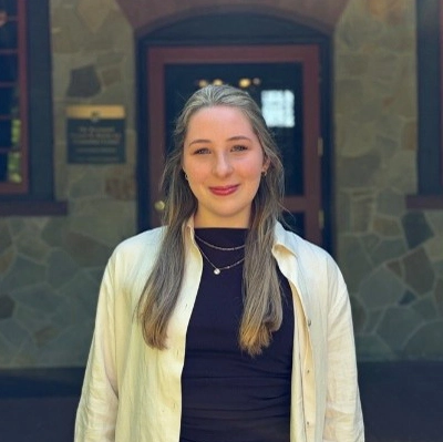 Meredith smiles by a large stone wall on the Humanities Building