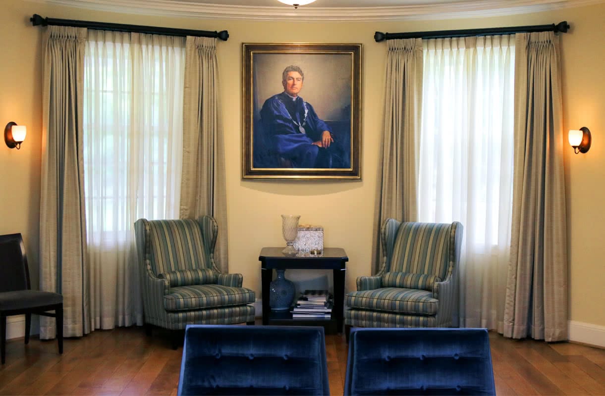 A painting of Brian Linnane hung on a tan wall, flanked by two windows