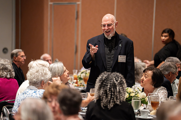 Alumni Chaplain Rev. Bill Rickle, S.J., '70, points in recognition to a fellow Golden Greyhound while circulating among tables at the luncheon