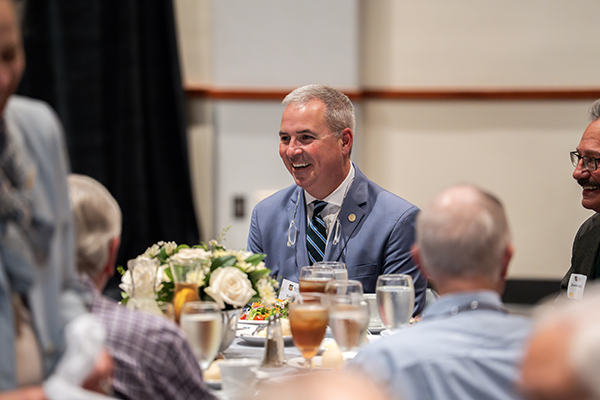 President Terrence M. Sawyer, J.D., smiles while enjoying lunch at a table surrounded by Golden Greyhounds