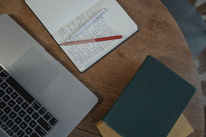 A laptop, notebooks, and pens spread out on a desk