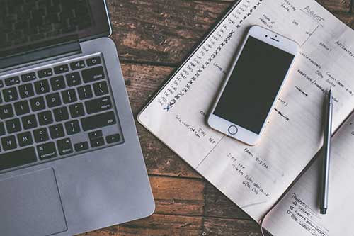 A laptop, iphone, and notebook open on a table