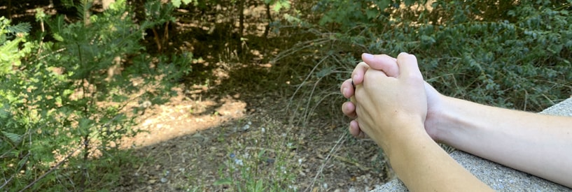 Folded hands leaning on a ledge overlooking nature