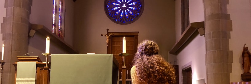 A student praying/reflecting at the alter of a chapel.