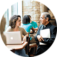 A student and a priest confer in a beautifully lit area of campus