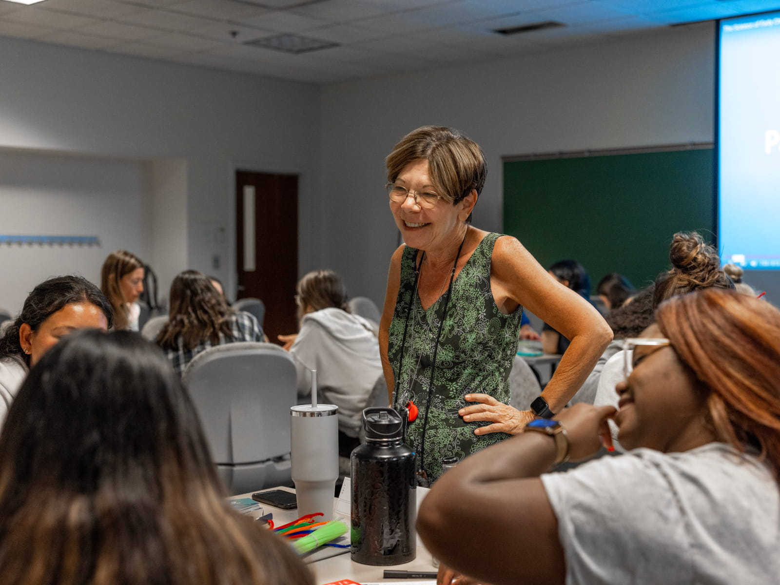 A member of coaching staff smiling while overseeing students working in a classroom