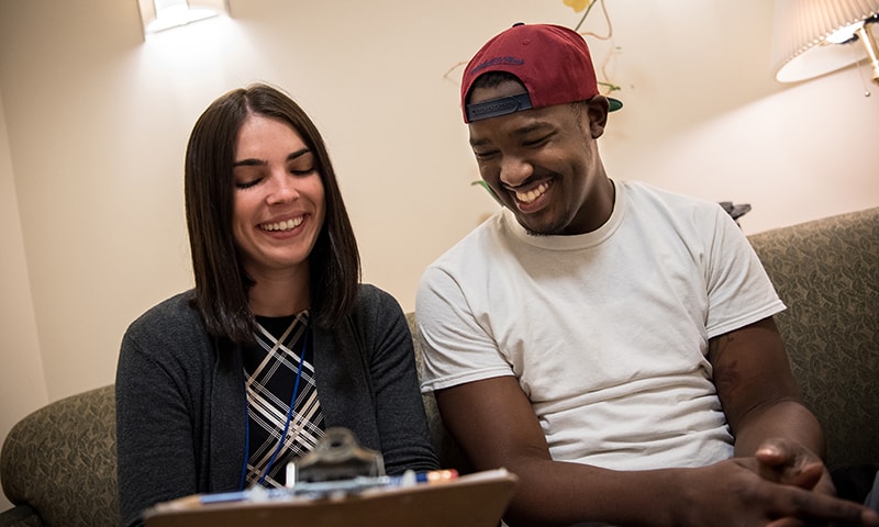 A client and Clinical Centers staff member sitting on a couch smiling and looking at a clipboard